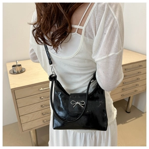 Détail d'un sac sous les aisselles en cuir verni noir avec boucle nœud en métal argenté