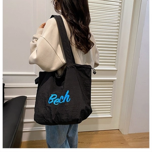 Détail du grand sac cabas noir avec lettrage bleu et fermeture latérale par cordon de serrage