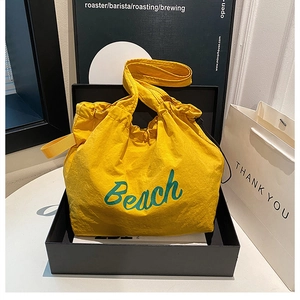 Détail d'un sac cabas jaune à cordon avec texte Beach vert dans une boîte cadeau