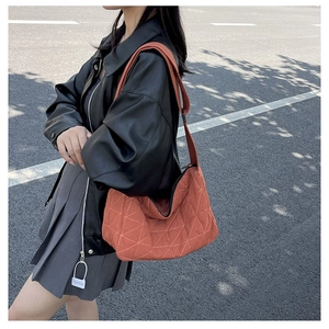 Detail of the orange quilted dumpling bag with triangular stitching on a street model