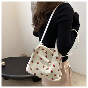 Detail of strawberry print corduroy tote bag worn by a model in a minimalist room