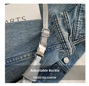 Détail de la boucle en métal réglable et de la sangle gris argent sur denim bleu