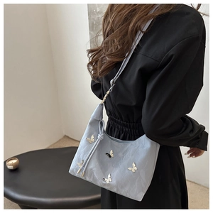 Détail du sac à bandoulière bleu clair avec tissu texturé et breloques papillons argentées