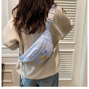 Detail of light blue waist bag featuring star patches and white rope fringe tassels