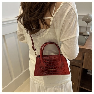 Detail of red crocodile pattern crossbody bag featuring gold lettering and leather texture