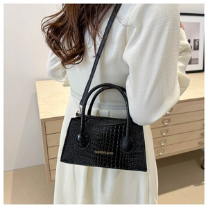 Detail view of black crocodile pattern handbag with gold lettering on a shoulder strap