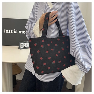 Détail du sac cabas en velours côtelé noir avec motifs fraises rouges et anse robuste