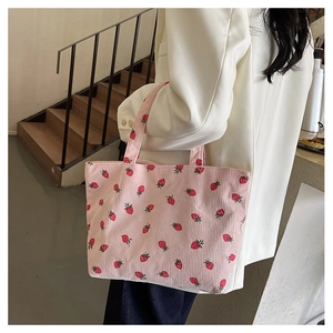 Sac fourre-tout en velours côtelé rose à motifs fraises porté à l'épaule par un mannequin