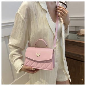 Close-up of pink quilted crossbody bag with a decorative pearl butterfly clasp on a model