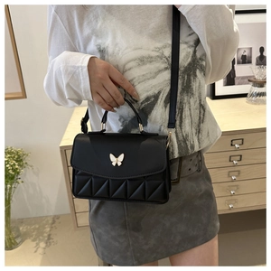 Detail of a black quilted crossbody bag with white butterfly metal hardware buckle