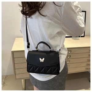 Detail of black leather square bag featuring a delicate white butterfly clasp and stitching