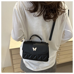 Detail of black quilted shoulder bag with white butterfly buckle worn by a model