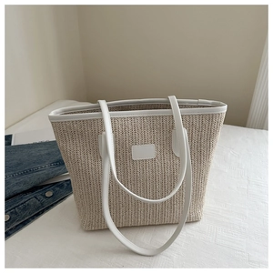 Détail du sac cabas en paille tissée beige avec bandoulière en cuir blanc sur lit blanc