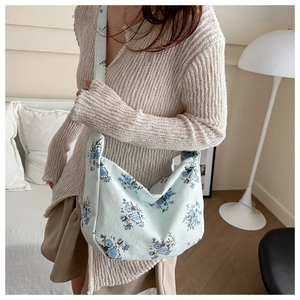 Detail of light blue corduroy crescent bag with floral print and wide strap on model