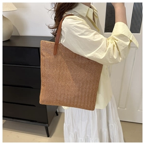 Detail of a woven straw tote bag with brown leather handles worn on the shoulder
