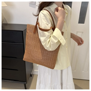 Detailed view of hand-woven straw tote bag with brown leather handles on model