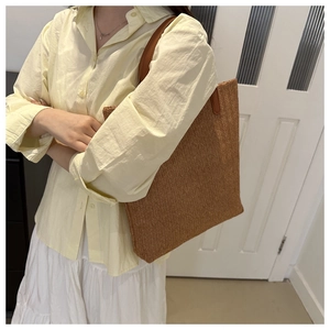 Detail of the woven texture and brown leather strap on a large straw tote bag