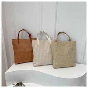 Detailed view of handmade woven straw tote bags with leather handles in three neutral colors