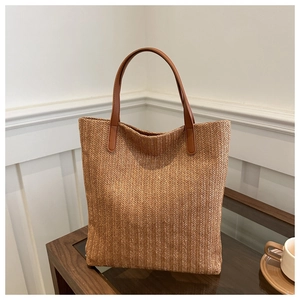 Detail of woven straw tote bag with brown leather handles on a dark wood table