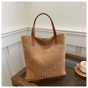 Detailed close-up of woven straw texture and brown leather handle of a large tote bag