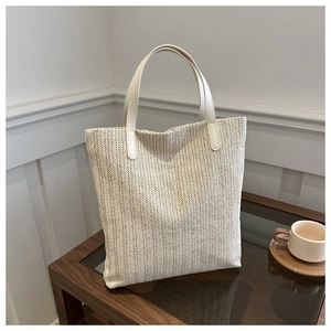 Detail of herringbone weave texture and leather handles on a beige woven tote bag