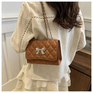 Detail of a brown quilted crossbody bag with a silver bow ornament and chain strap