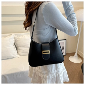 Detail of a black leather underarm bag with a gold metal clasp shown on a model