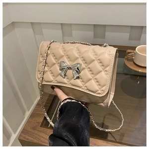 Gros plan du sac bandoulière matelassé beige avec nœud en argent et bandoulière chaîne