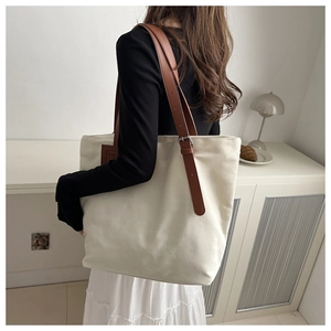 Close-up of cream canvas tote bag with adjustable brown leather straps and metal buckle