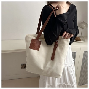 Close-up of cream canvas tote bag with brown leather strap and embossed logo detail