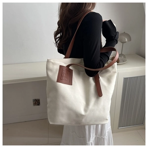 Detail of canvas tote bag showing brown leather logo patch and shoulder straps