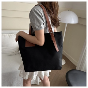 Detail view of black canvas tote bag with adjustable brown leather straps and metal buckle