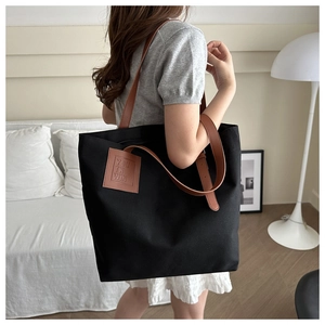 Close-up of black canvas tote bag with brown leather accents and embossed lettering