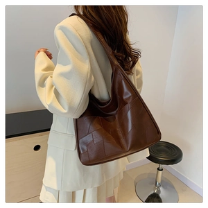 Brown leather tote bag worn by model showing large capacity and geometric design