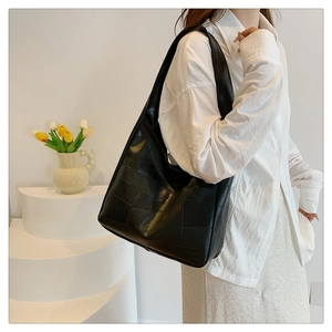 Detail of black patchwork leather tote bag showing geometric texture and side profile