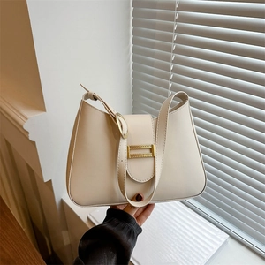 Minimalist beige leather shoulder bag with gold buckle shown in a modern home setting