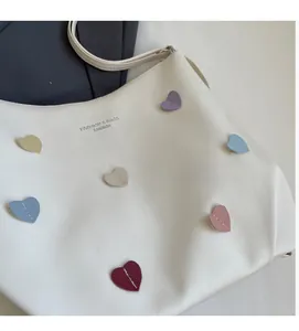 Detail of white tote bag featuring colorful heart patches and cross-grain PU texture