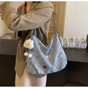 Detail of light blue denim hobo bag with colorful heart patches and cloud charm