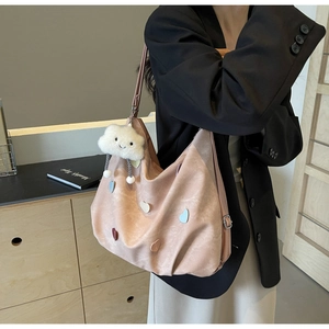 Detail of a dusty pink tote bag with heart patches and cloud charm on a shoulder strap