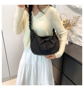 Side view of black pleated nylon shoulder bag with drawstring closure on model