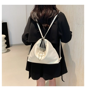 Detail of a creamy white pleated backpack with elegant metal chains and pearl charms decor