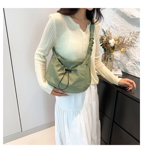 Close-up of green nylon crossbody bag with drawstring closure and pleated strap details