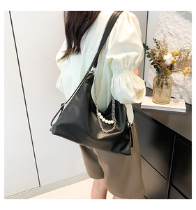 Detail of black leather shoulder bag with decorative pearl charm and silver chain strap