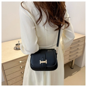 Black leather crossbody bag with gold metal H-buckle detail shown on a model