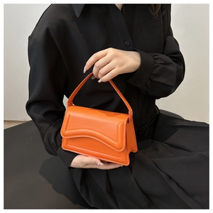 Detailed close-up of a bright orange leather handbag with wavy flap and matching stitching