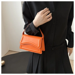Macro detail of vibrant orange rectangular handbag with wavy flap and fine stitching