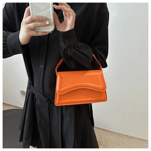 Detail of stylish orange patent leather handbag featuring unique wave-cut edge design