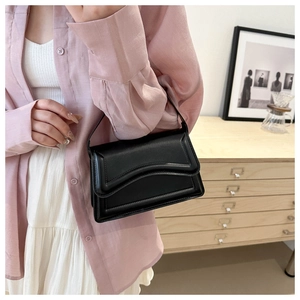 Detail of a black PU leather handbag with wavy flap edge held against a soft background