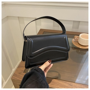 Close-up of a black matte leather handbag featuring a unique wavy flap design and wide strap