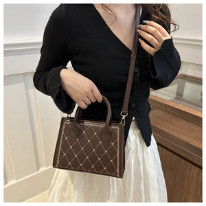 Detail of dark brown handbag featuring cream quilted embroidery and small heart accents